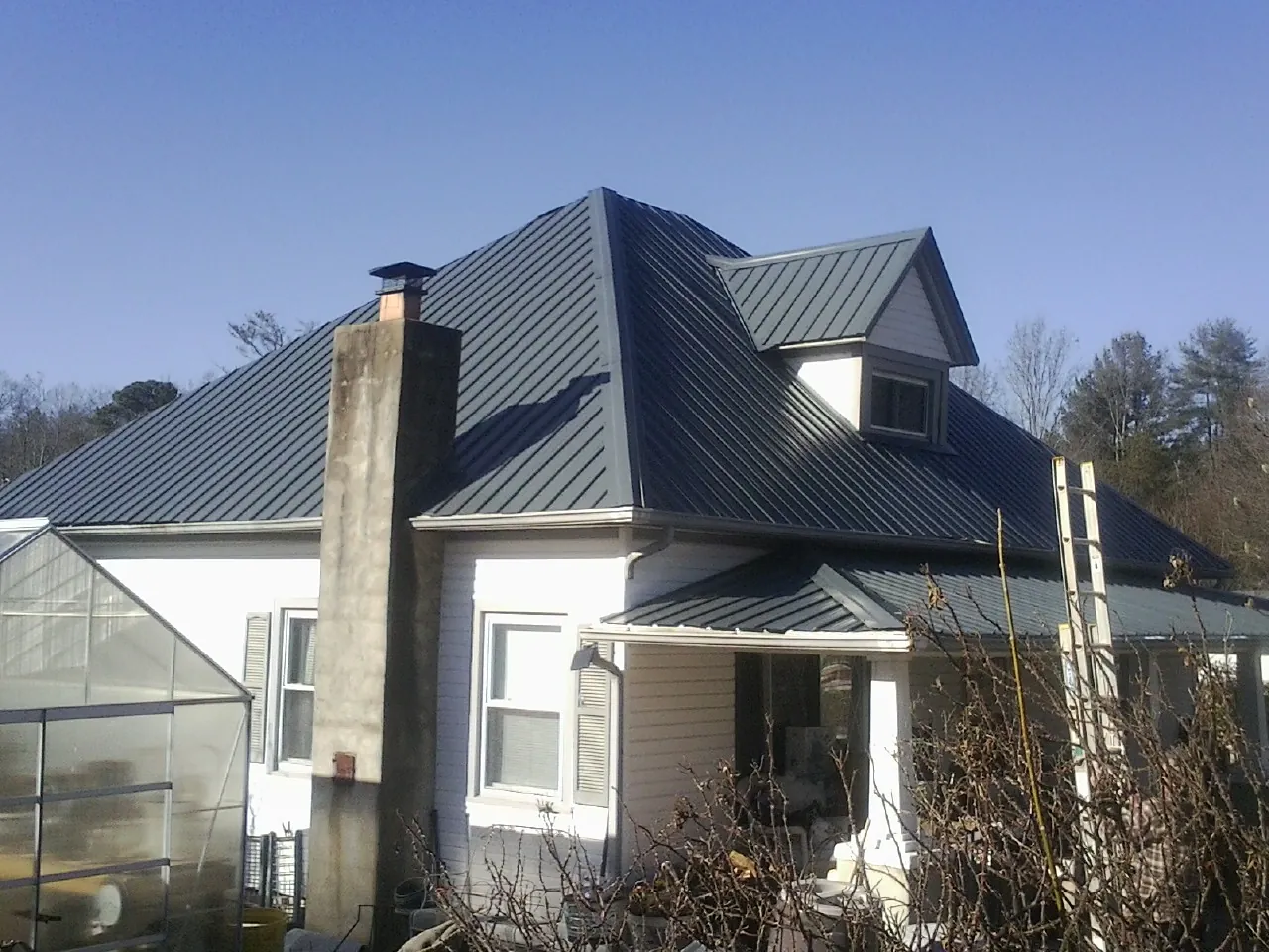 Dark blue standing seam metal roof on a white farmhouse with dormer — Slate & Tile Roof Repair by Roofing Brothers in Clermont