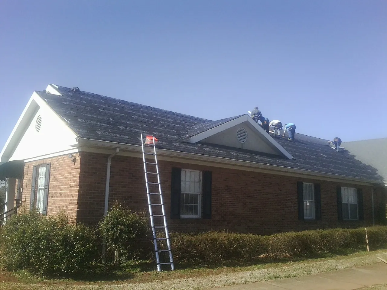 Crew tearing shingles off a brick ranch roof with a ladder set — Metal Roof Repair work by our crew in Clermont