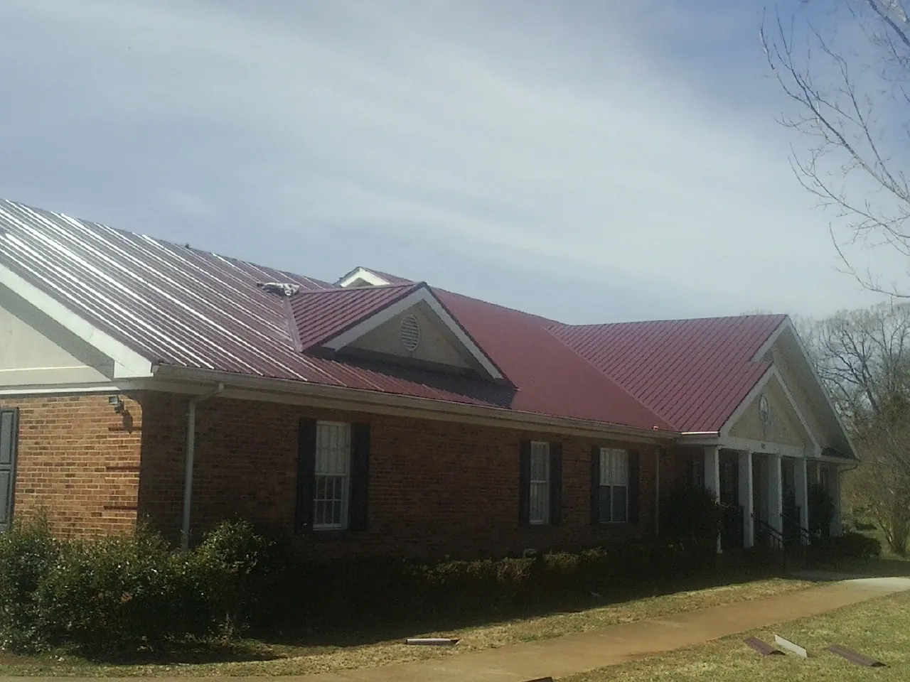 Red metal roof with gabled entries on a long brick building, from a Hail Damage Roof Repair job in Clermont