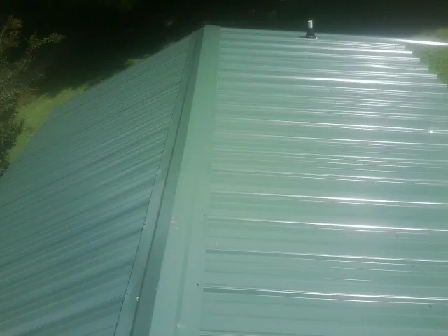 New green metal panels meeting at the ridge of a roof — Flat Roof Repair work by our crew in Clermont