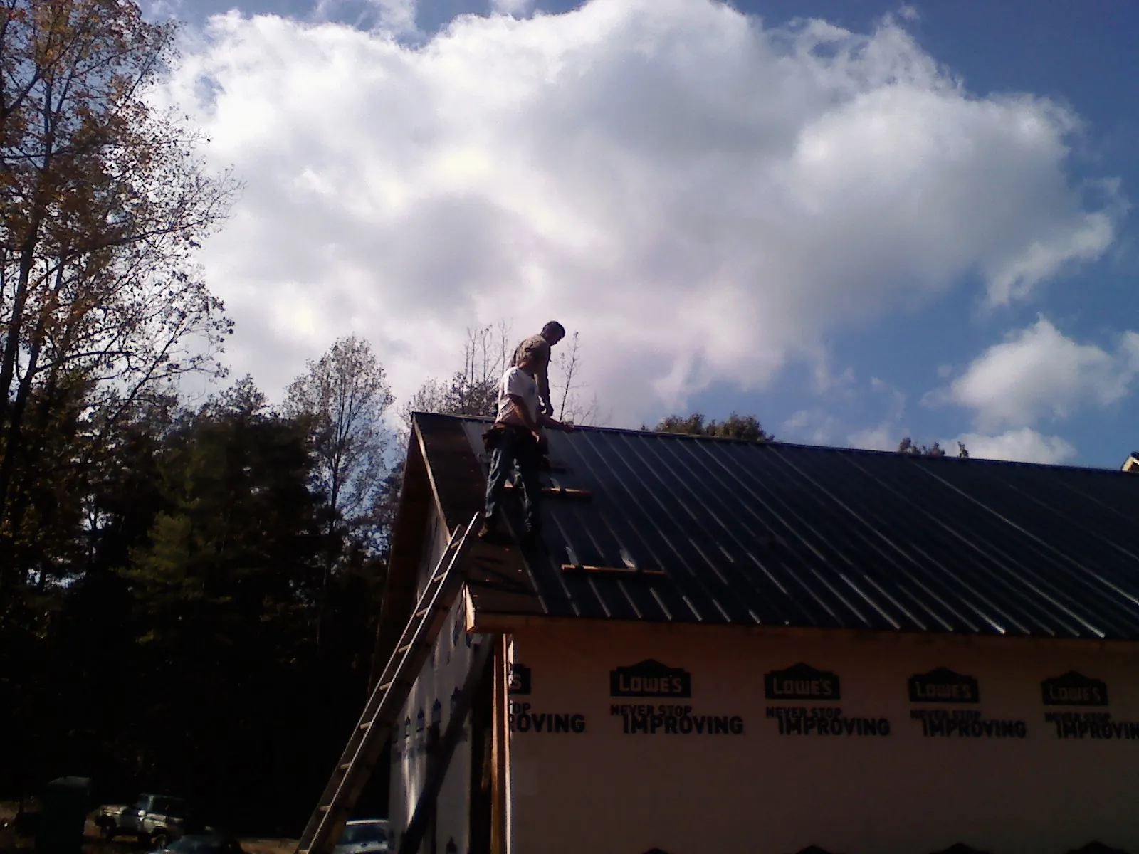 Roofer fastening dark metal panels high against a cloudy sky, from a Roof Inspection job in Clermont